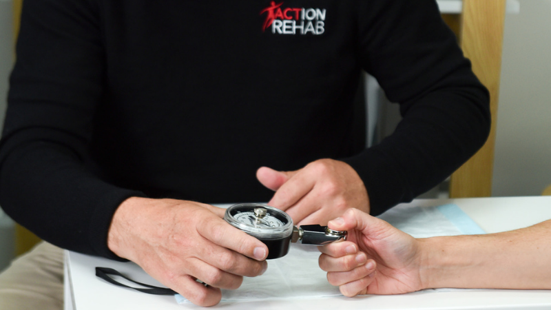Hand therapist measuring thumb pinch strength using a pinch gauge during thumb injury rehabilitation at Action Rehab - The Hands Physio.
